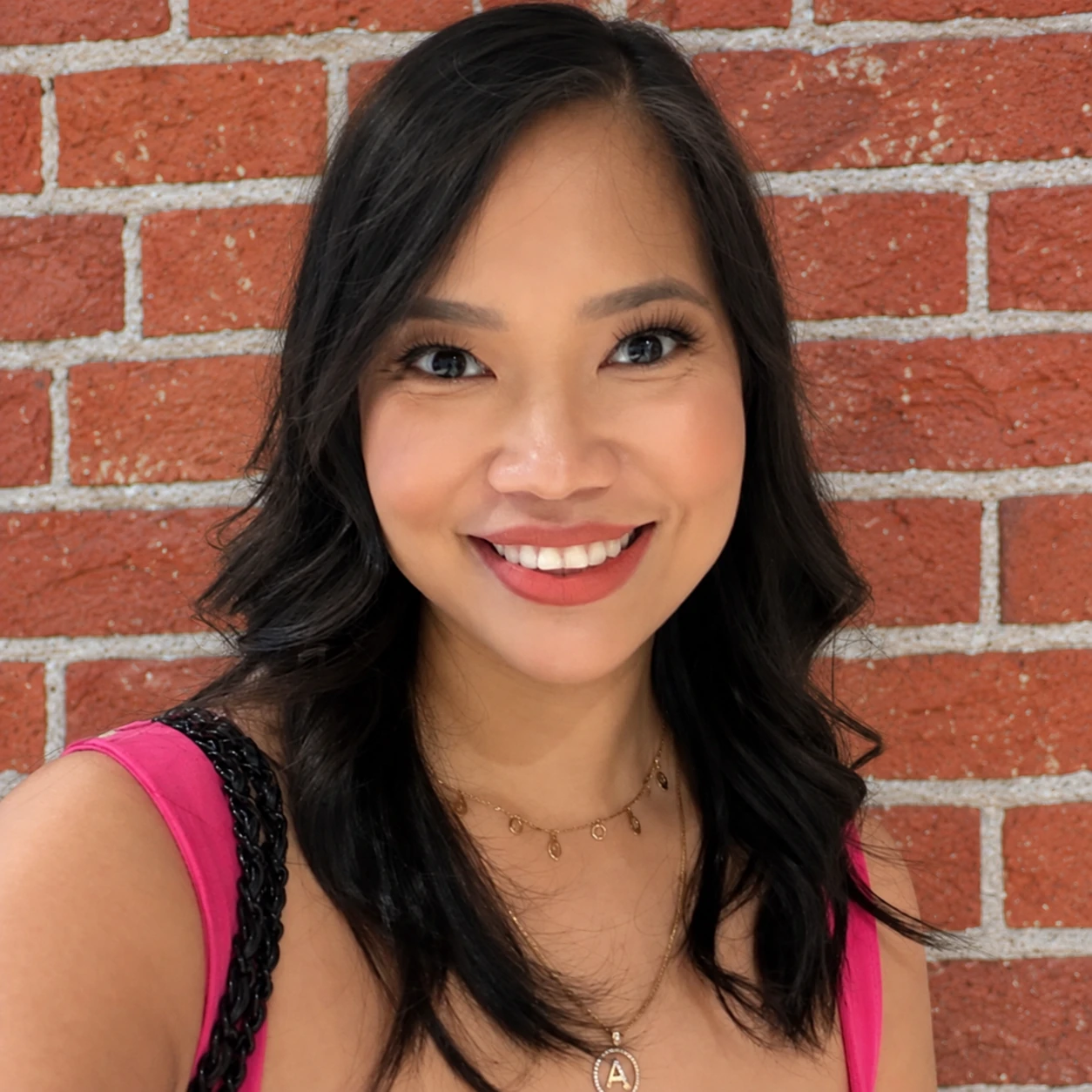 Annikka Aborro smiling in a bright pink top beside a red brick wall